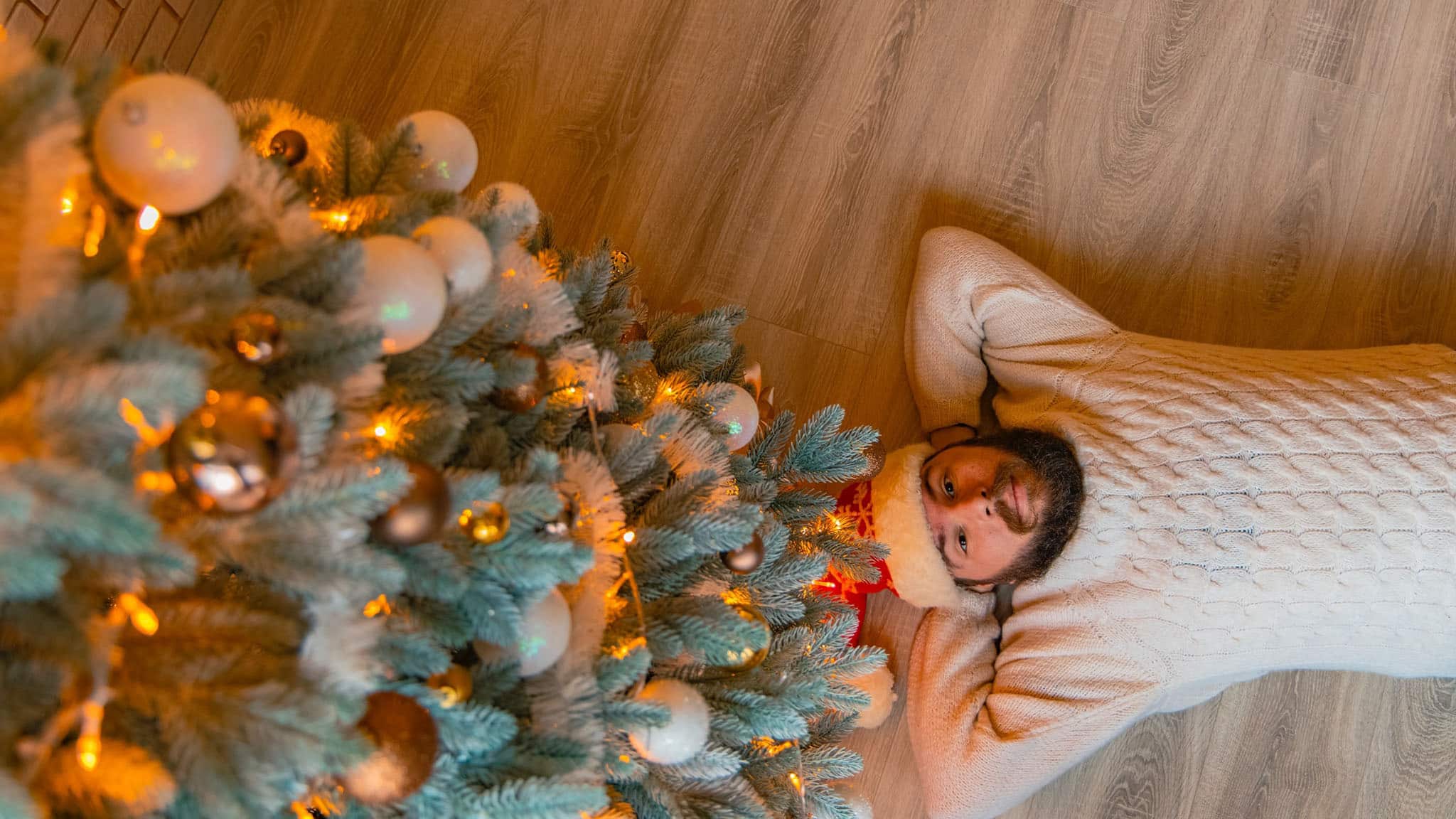 Aerial Photograph Of Man Laying On Wooden Floor Beside Lit Christmas Tree