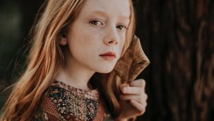 Photograph Of Thoughtful Young Girl Holding Brown Autumn Leaf In Hand Near Her Face