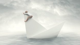 A Conceptual Image Shows A Paper-Like Sailboat In The Water With A Man Clinging To The Topmost Sail Against A Gray Cloudy Sky