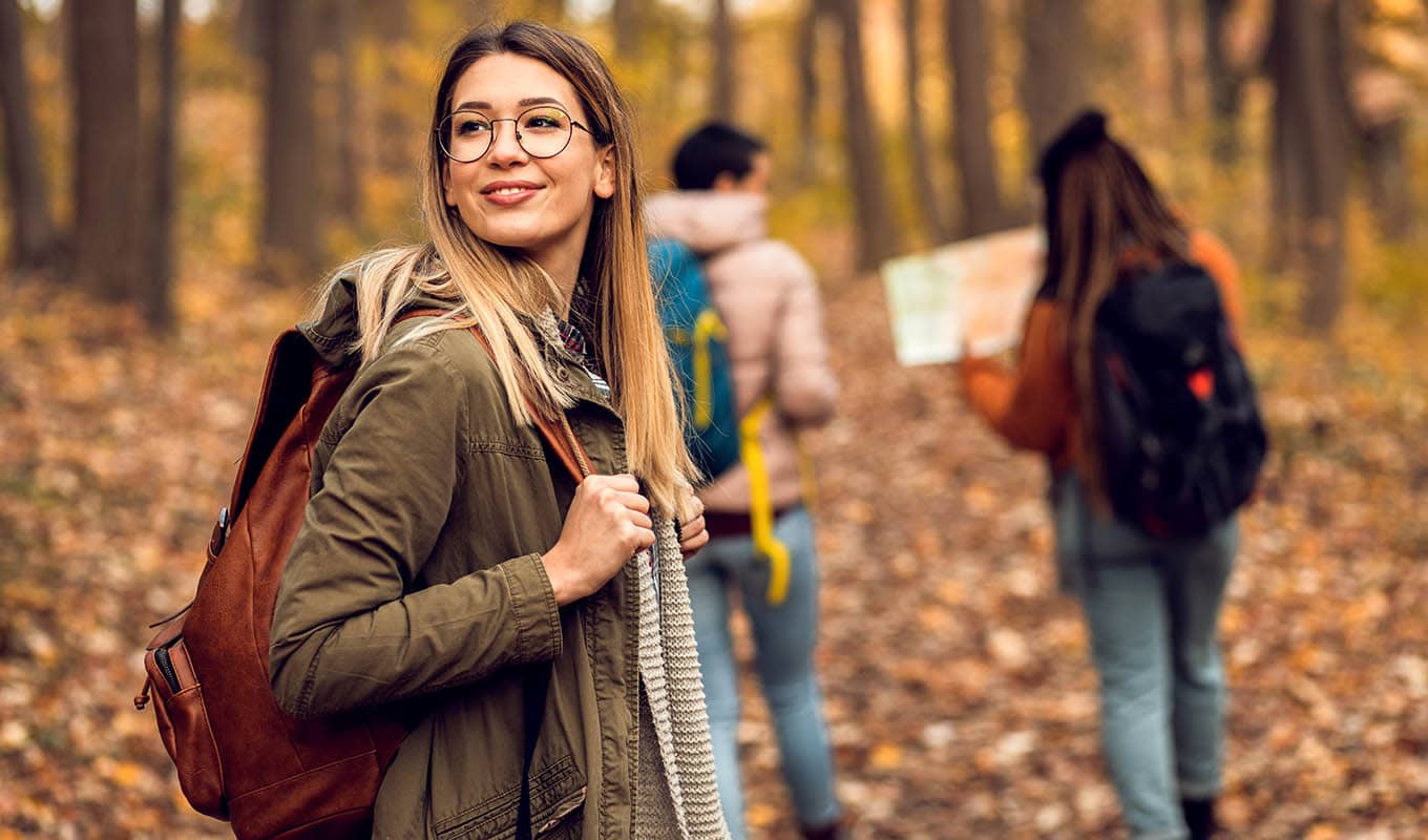 Photograph Of Woman Smiling While Walking Through Autumn Forest With Friends