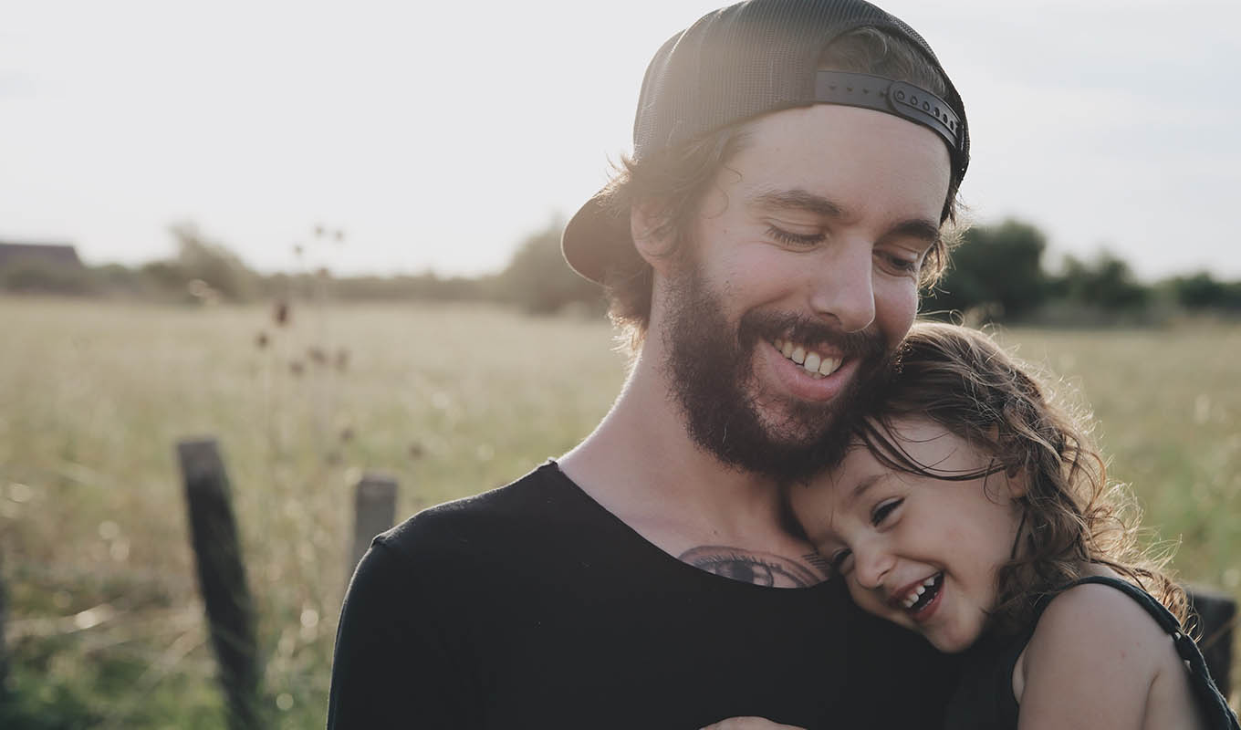 Closeup Photograph Of Smiling Man Holding Laughing Toddler While Standing In A Grassy Field