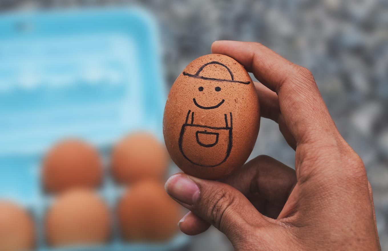 Close Up Photograph Of Hand Holding An Egg With A Smiley Face Drawn On It