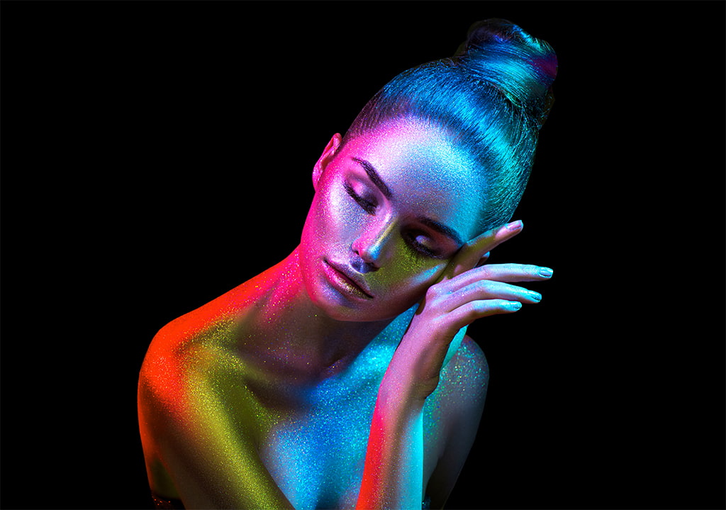 attractive model wearing glittery makeup shining in rainbow colors against a black background