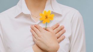 Photograph Of Hands Resting Over Heart While Holding Bright Yellow Flower, Hope And Love Concept