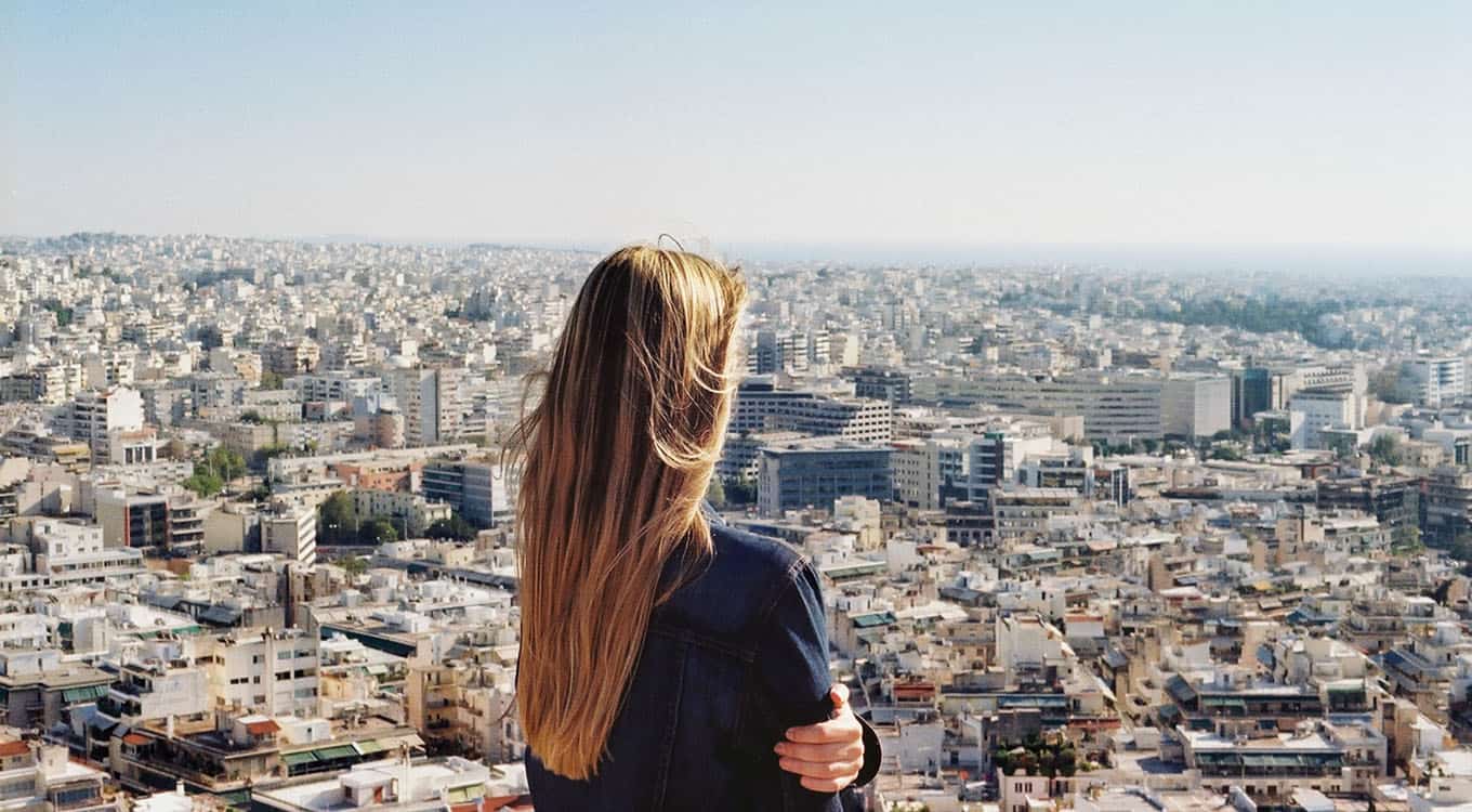 Rear View Photograph Of Caucasian Woman Hugging Herself And Looking Over A Vast Cityscape