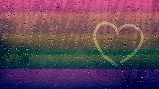 Finger-Drawn Heart Shape On Rainy Window Surface With A Rainbow Cast