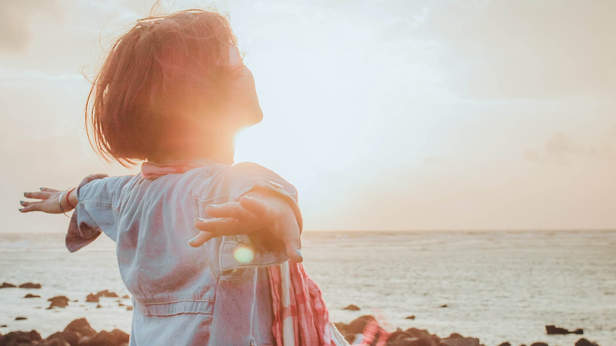 Getting To The Heart Of Loneliness & Depression During COVID Rear View Photograph Of Woman Facing Sunrise On Beach With Arms Outstretched, Hope Concept