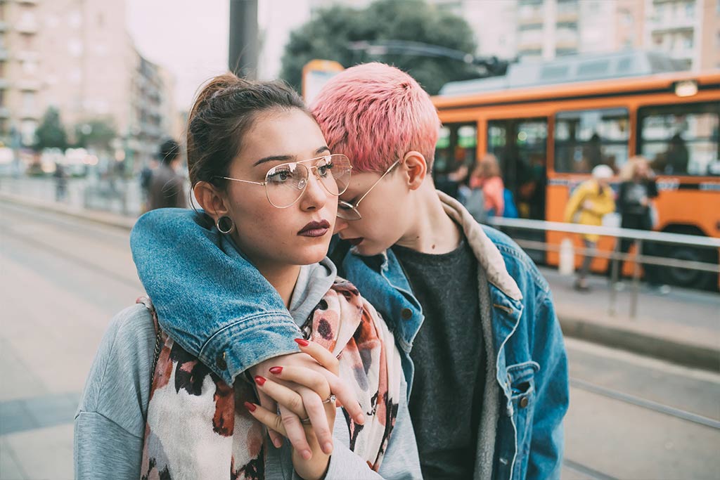Photograph Of Young Woman With Her Arm Around The Shoulders Of Another Woman As They Walk Down A City Street