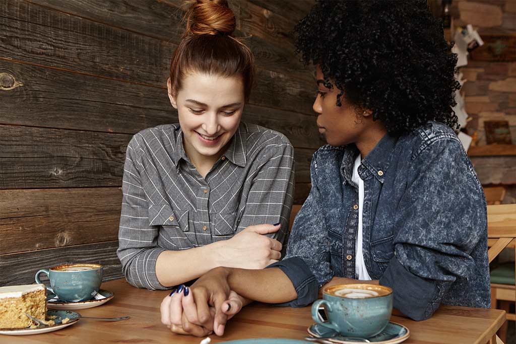 Photograph Of Interracial Lesbian Couple Sitting Together In A Cozy Coffee Shop