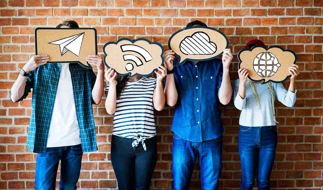 photo of four young people holding cardboard cutouts of internet symbols over their faces pointing towards modern technology as a contributing factor to their loneliness and isolation from each other