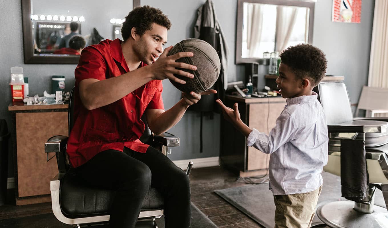 photograph of a young man teaching an only child boy how to handle a basketball to help the boy not feel lonely