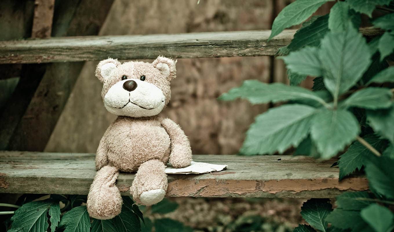 photograph of smiling stuffed bear sitting on outdoor bench, feeling content with life while getting over the loneliness of a breakup