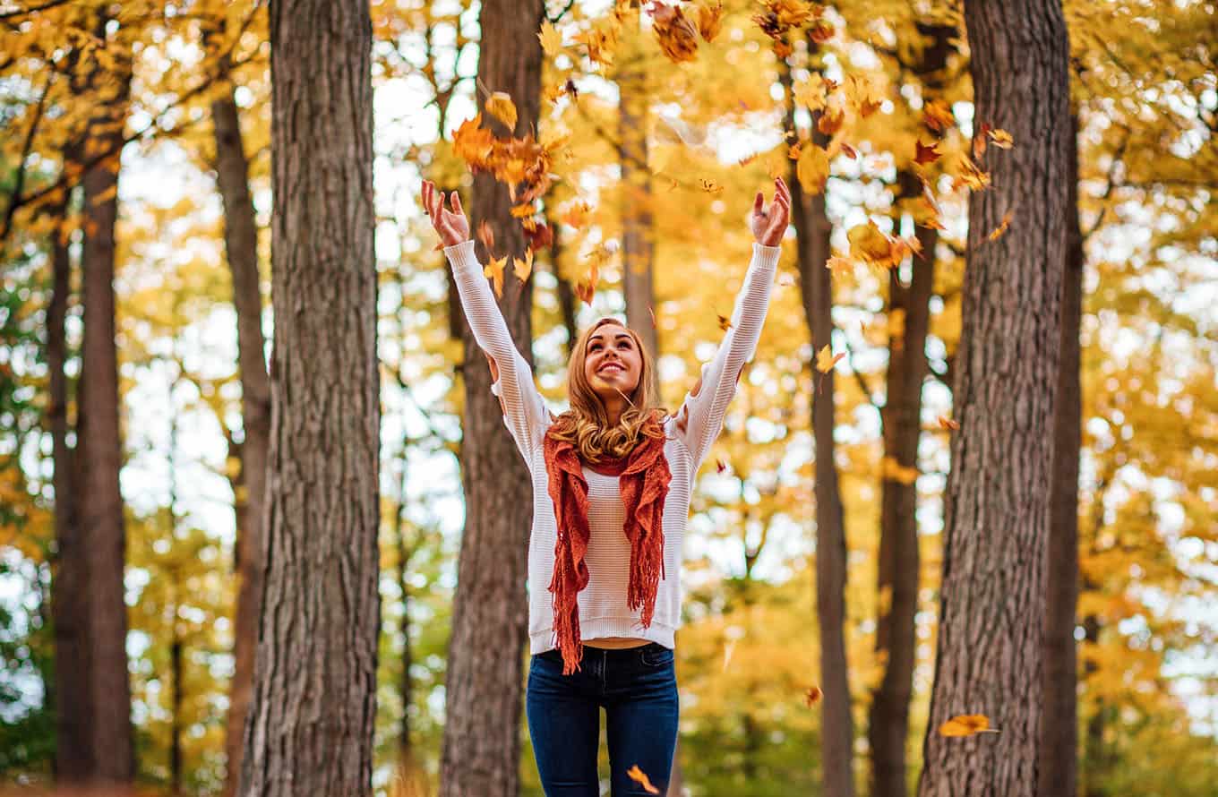 Photograph Of Happy Young Woman Standing Alone In Autumn Forest Throwing Leaves Overhead, Joy Concept