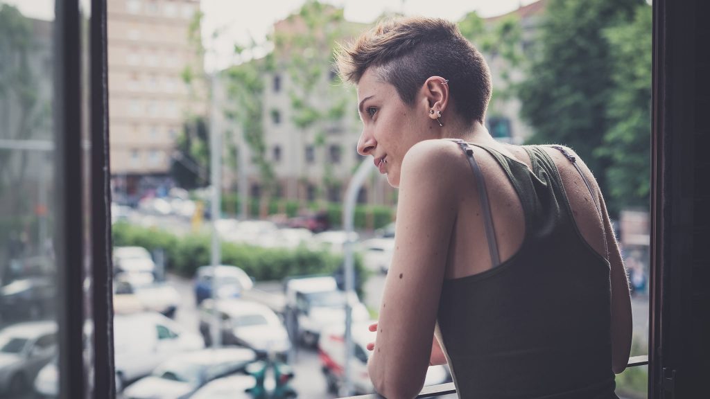 photograph of a woman looking outside from a balcony while living alone