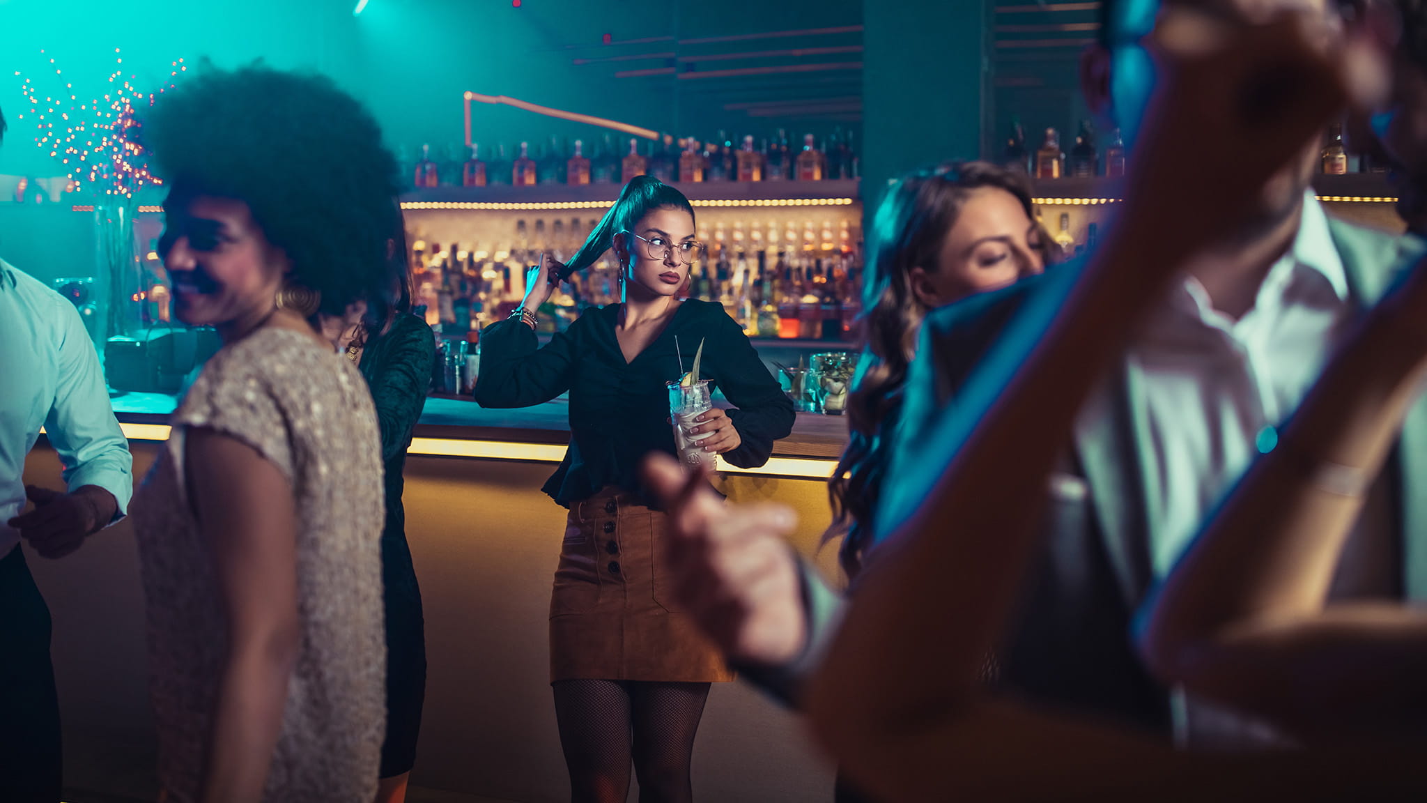 Moody Photograph Of Woman Leaning On A Bar, Surrounded By Others But Feeling Alone