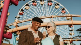 Aged Photograph Of Multi-Racial Older Couple Eating Cotton Candy With Ferris Wheel In Background