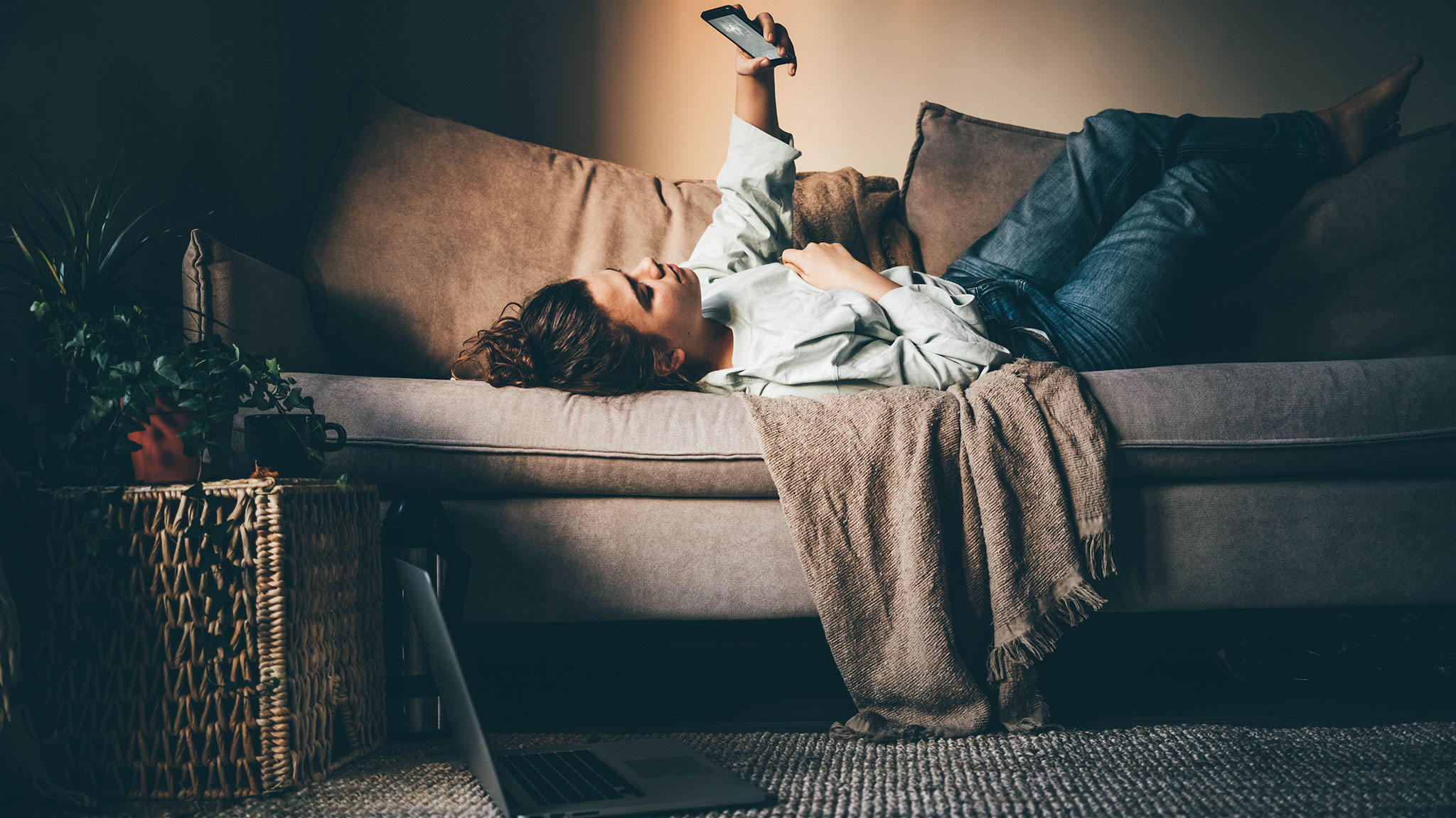 Moody Photograph Of Woman Laying On Couch While Staring Upward At Phone Screen, Endless Boredom Concept