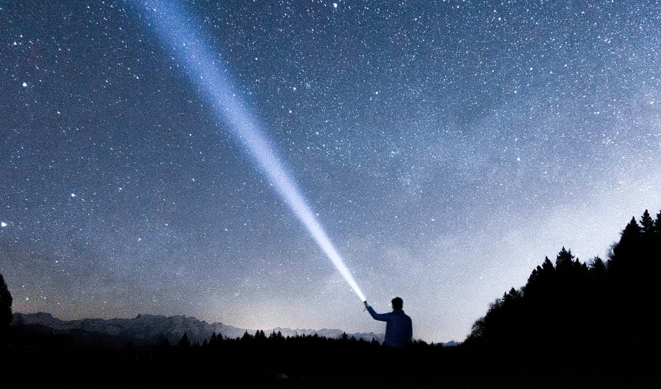 photograph of person shining a flashlight into the night sky