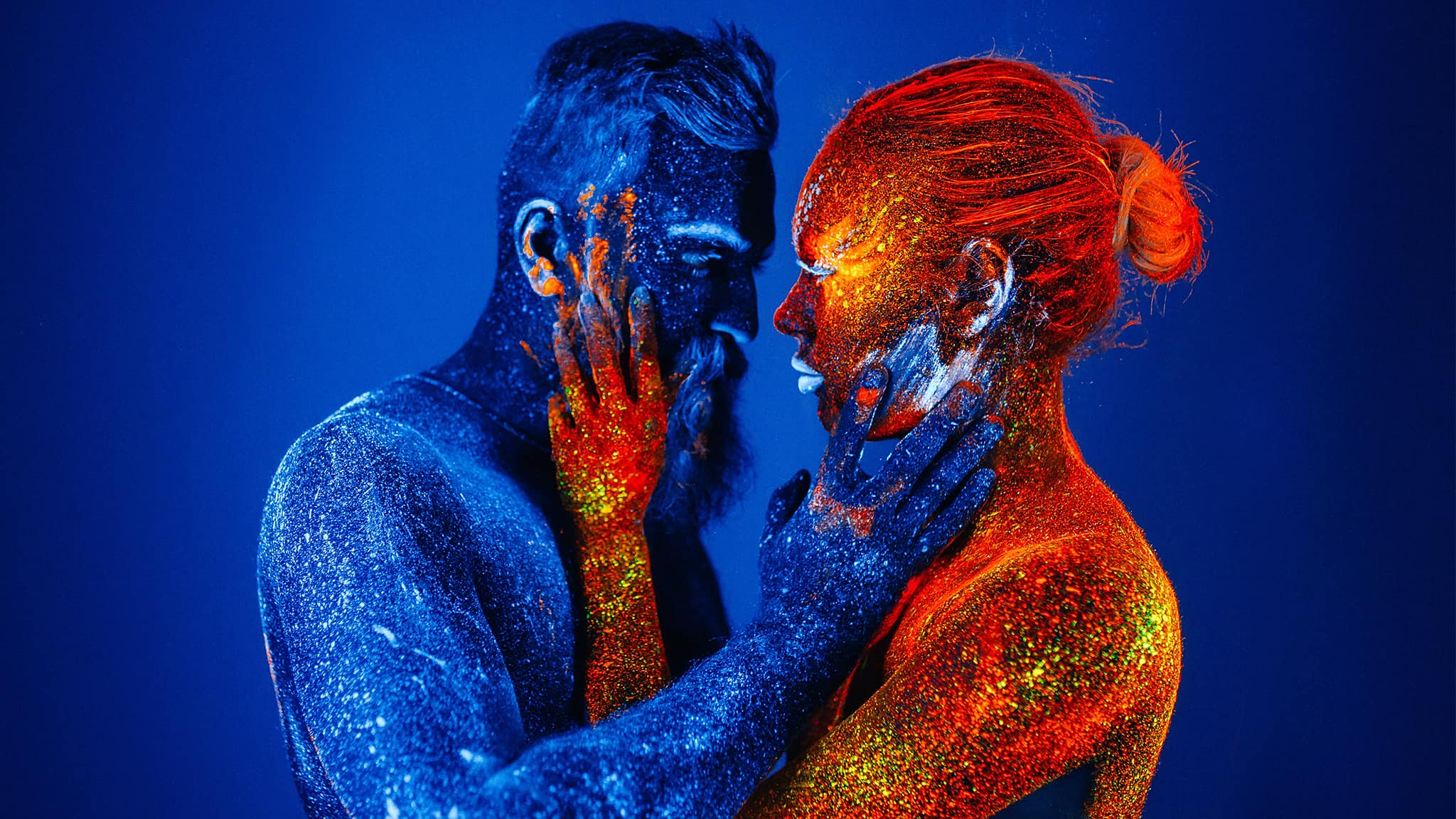 Bearded Man In Blue And Woman In Red In Ultraviolet Powder Looking Into Each Other's Eyes Signifying A Soulmate Or Twin Flame