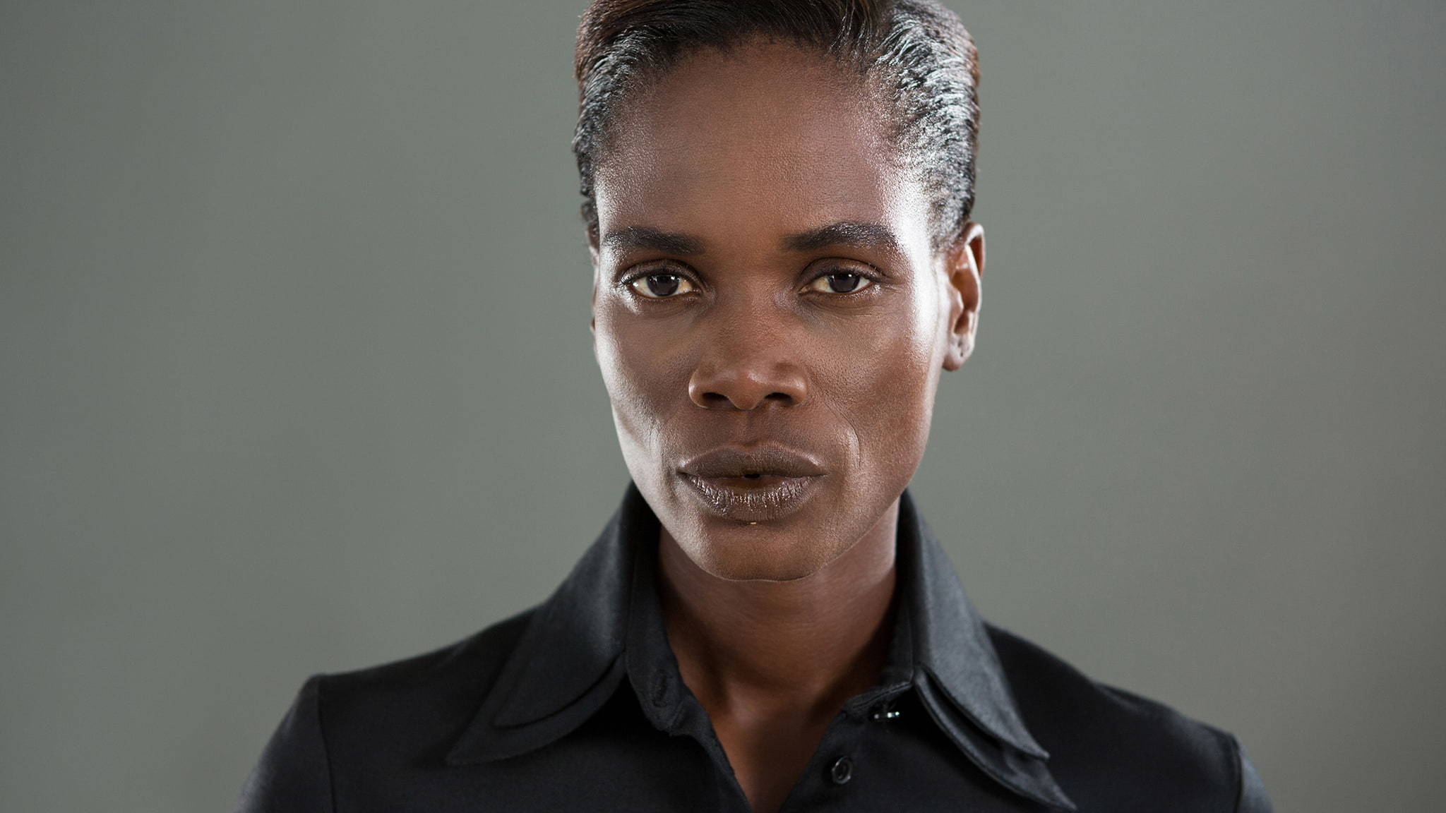 An African American Androgynous Person Wearing A Black Collared Shirt With A Serious Look On Their Face