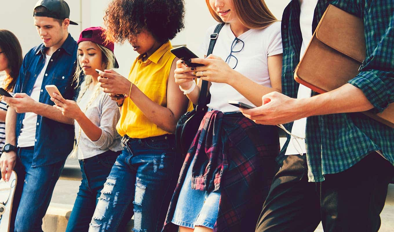 Photograph Of Several Young People Of Varied Genders Standing Together While Staring At Their Mobile Phones