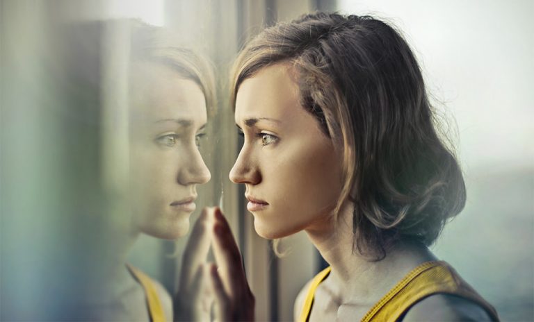 a young woman staring out a college down window while experiencing bpd loneliness