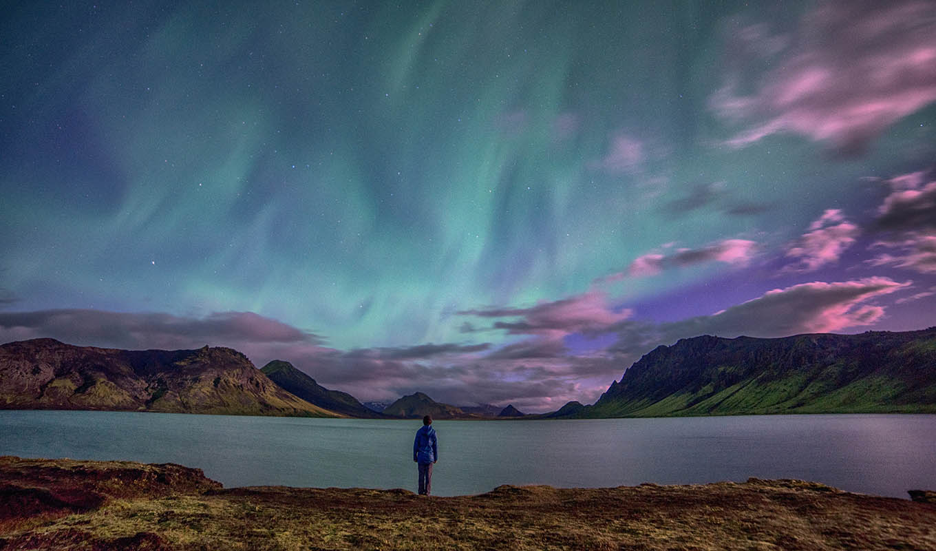 photograph of man standing and watching the aurora borealis, experiencing cosmic loneliness