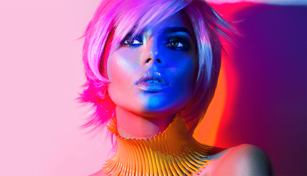 model in pink and purple lighting wearing metallic makeup and striking a pose