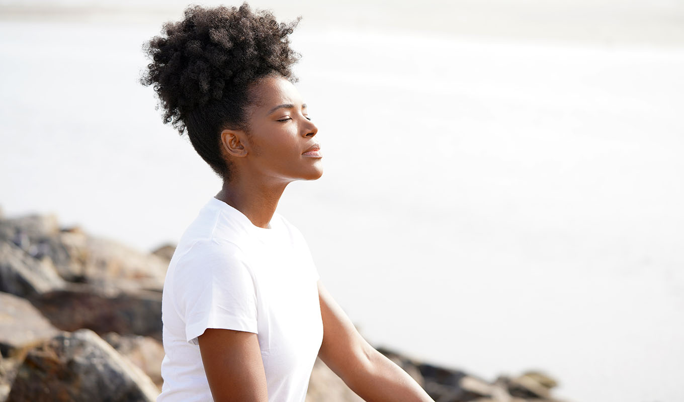 Photo Of Black Woman With White T-Shirt Sitting On Rocks Meditating With Eyes Closed