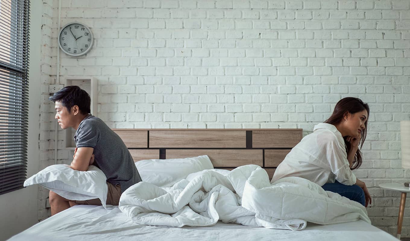 photo of man and woman sitting on the bed facing opposite directions, feeling lonely in their relationship