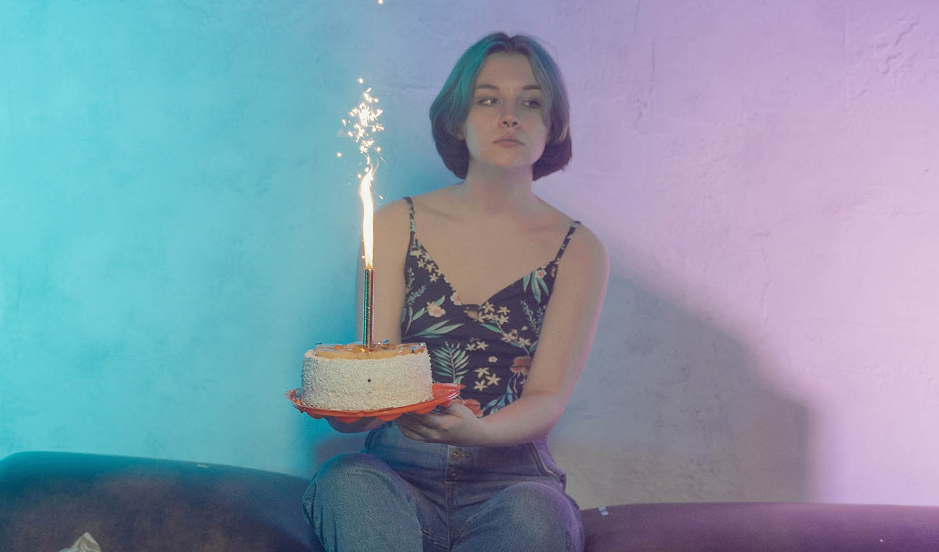 Photograph Of Unimpressed Young Woman Holding A Cake With Giant Lit Sparkler As A Candle