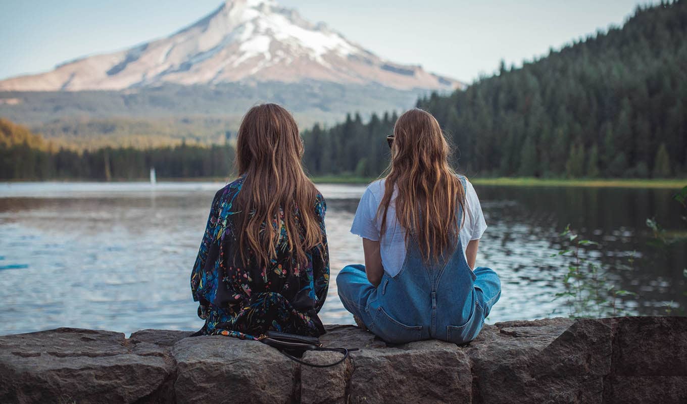 photograph of two female friends sitting together while facing the lake, experiencing loneliness separately