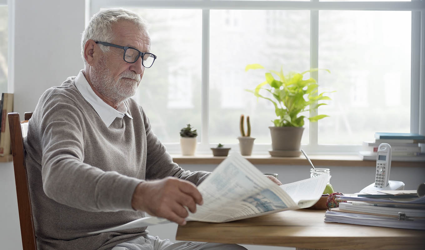 Photograph Of Senior Man Reading Newspaper Alone At Kitchen Table