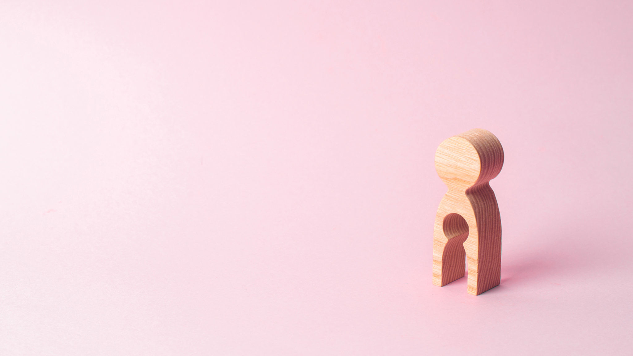 Coping With The Grief Of Miscarriage Is Very Difficult But You Are Not Alone Wooden Peg Shaped Like A Person With A Smaller Identical Peg Missing Inside Of It Against a Plain Pink Background Symbolizing A Woman Missing A Child From Miscarriage